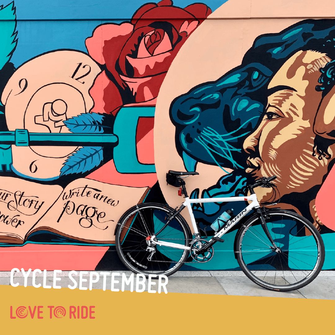 A bike propped up against a wall covered in a large colourful mural which contains images of faces, a key, and an open book containing the words ‘your story your power, write a new page’. The text on the asset says ‘what’s your ride for Cycle September?’. A bike propped up against a wall covered in a large colourful mural which contains images of faces, a key, and an open book containing the words ‘your story your power, write a new page’. The text on the asset says ‘what’s your ride for Cycle September?’.