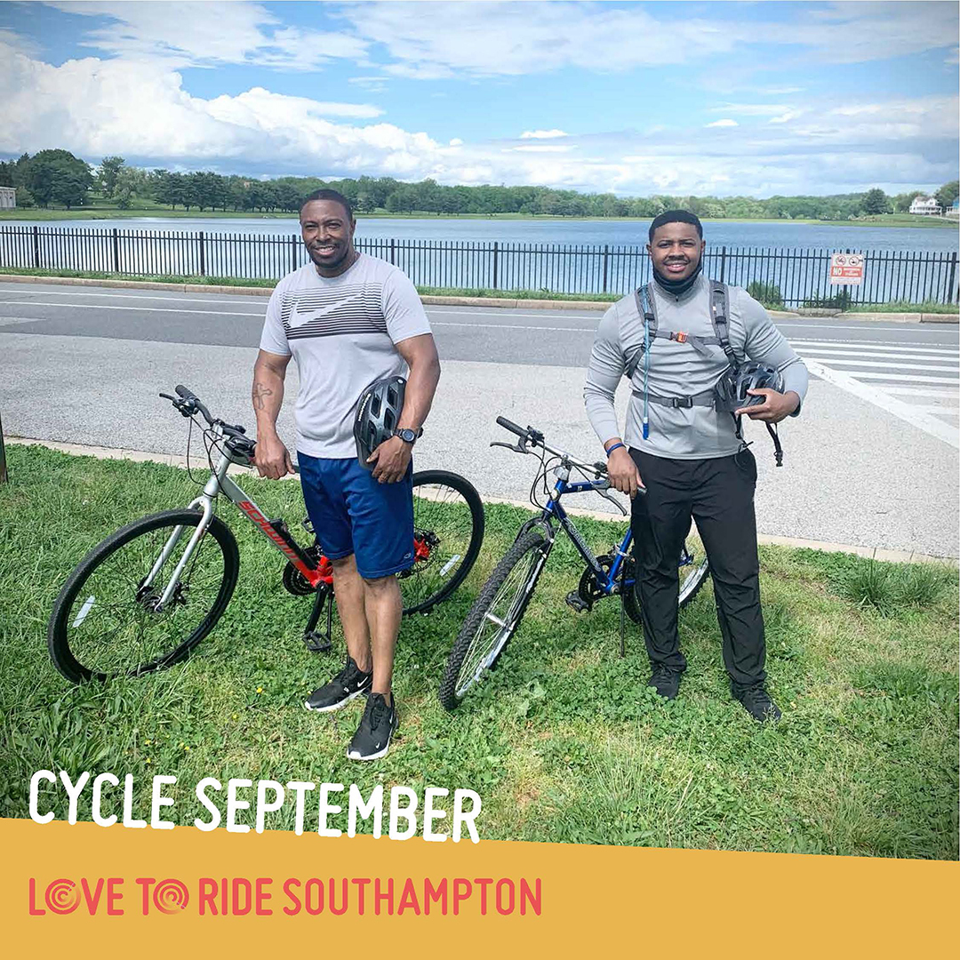 Two men stand with bikes on a grass verge next to a road and in front of a lake. They both hold helmets and are smiling. The text says ‘Cycle September’ and the Love to Ride logo is displayed. Two men stand with bikes on a grass verge next to a road and in front of a lake. They both hold helmets and are smiling. The text says ‘Cycle September’ and the Love to Ride logo is displayed.