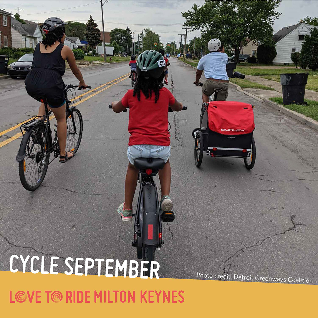 A family riding on a residential road, shown from behind. One person carries a trailer on their bike. The text says ‘Cycle September. Photo credit: Detroit Greenways Coalition’ and the Love to Ride logo is displayed. A family riding on a residential road, shown from behind. One person carries a trailer on their bike. The text says ‘Cycle September. Photo credit: Detroit Greenways Coalition’ and the Love to Ride logo is displayed.