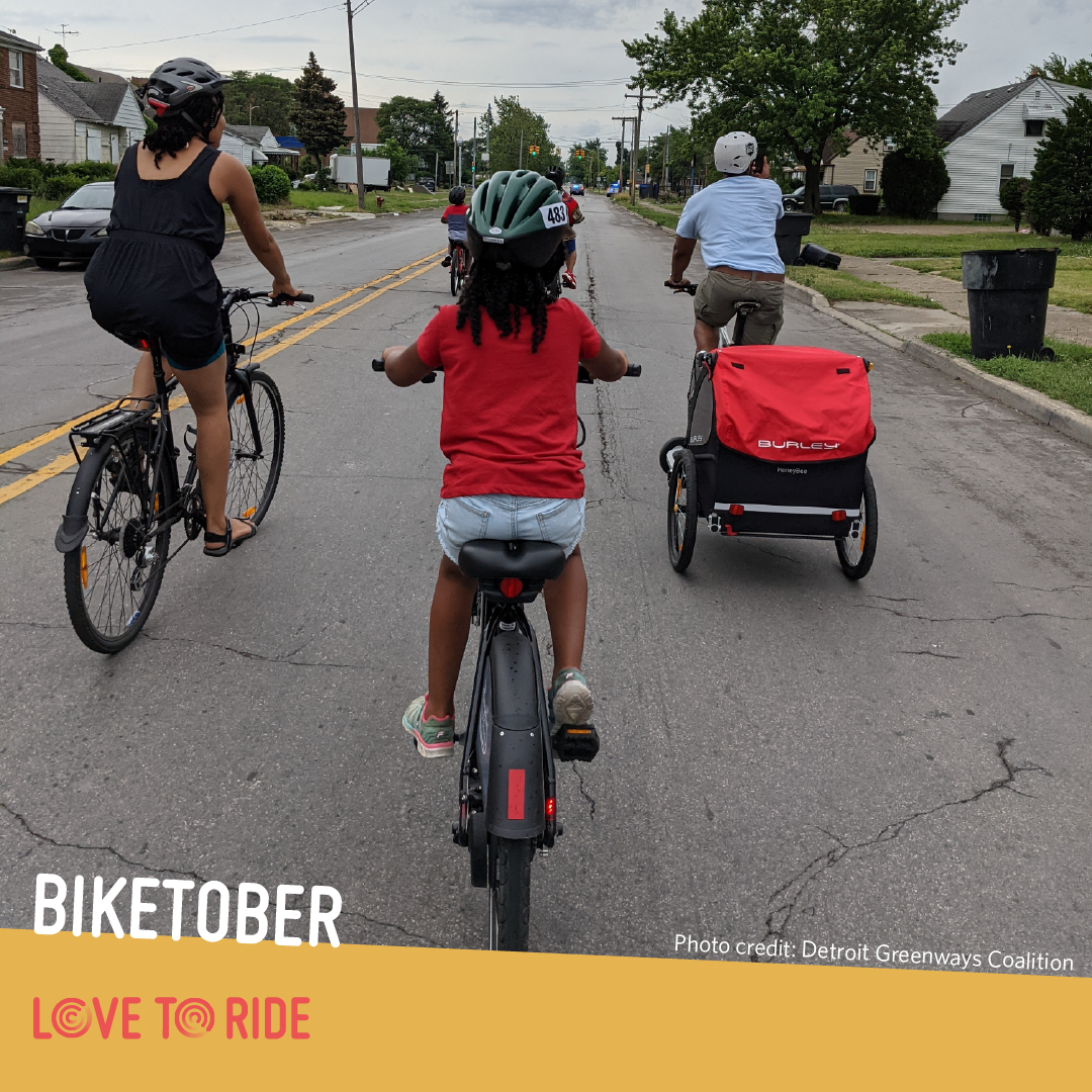 A family riding on a residential road, shown from behind. One person carries a trailer on their bike. The text says ‘Biketober. Photo credit: Detroit Greenways Coalition’ and the Love to Ride logo is displayed. A family riding on a residential road, shown from behind. One person carries a trailer on their bike. The text says ‘Biketober. Photo credit: Detroit Greenways Coalition’ and the Love to Ride logo is displayed.