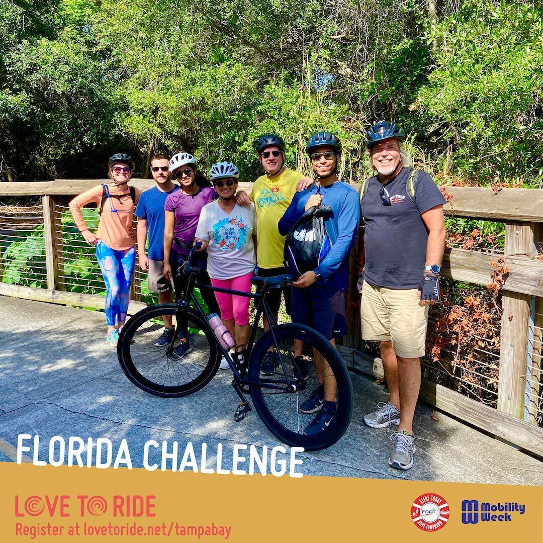 A group of riders stood with helmets on infront of trees. A woman at the front is holding a black bike so it stands. The text on the asset says ‘Florida Challenge’. The logos for Love to Ride, Alert Today and Mobility Week are at the bottom right corner. A group of riders stood with helmets on infront of trees. A woman at the front is holding a black bike so it stands. The text on the asset says ‘Florida Challenge’. The logos for Love to Ride, Alert Today and Mobility Week are at the bottom right corner.