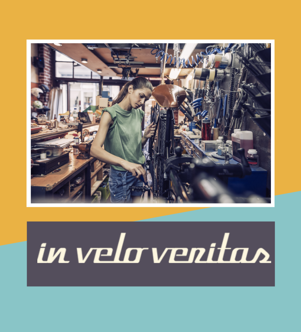 A bike mechanic working on a bike in a workshop. The In Velo Veritas logo is displayed below. A bike mechanic working on a bike in a workshop. The In Velo Veritas logo is displayed below.