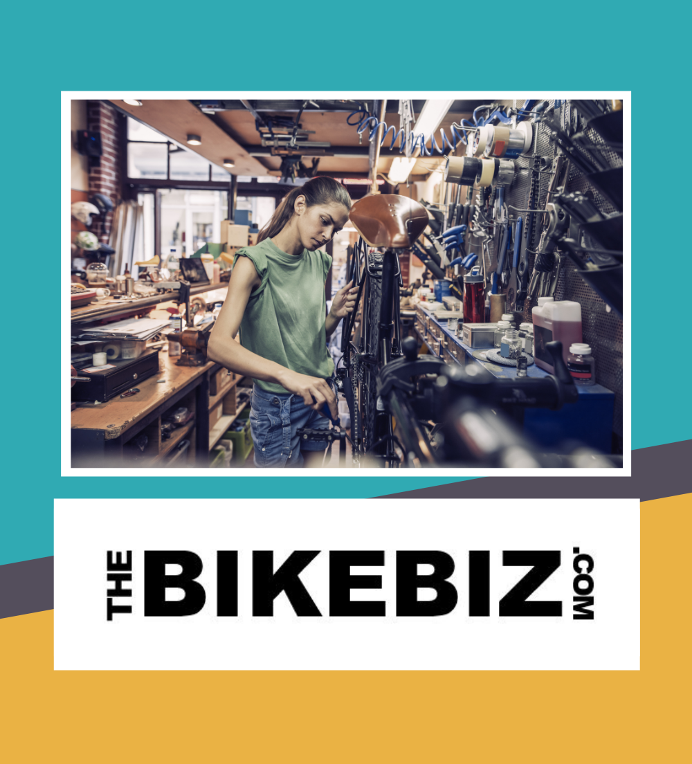 A bike mechanic works on a bike in a workshop. Below the Bike Biz logo is displayed. A bike mechanic works on a bike in a workshop. Below the Bike Biz logo is displayed.