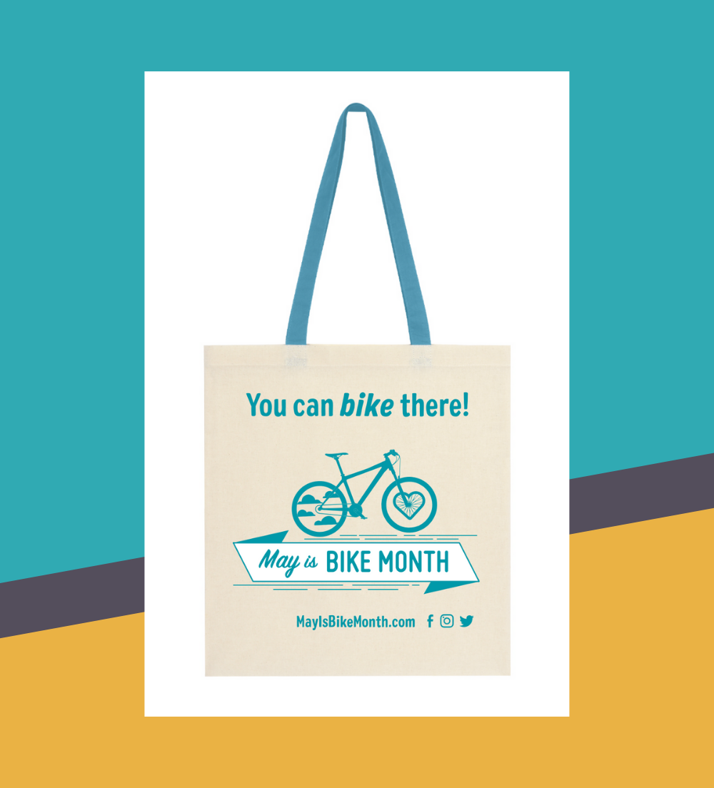 an off-white tote bag with a turquoise strap. The tote says "You can bike there" and has an image of a bike with the May is Bike Month banner. Below, the URL mayisbikemonth.com an off-white tote bag with a turquoise strap. The tote says "You can bike there" and has an image of a bike with the May is Bike Month banner. Below, the URL mayisbikemonth.com